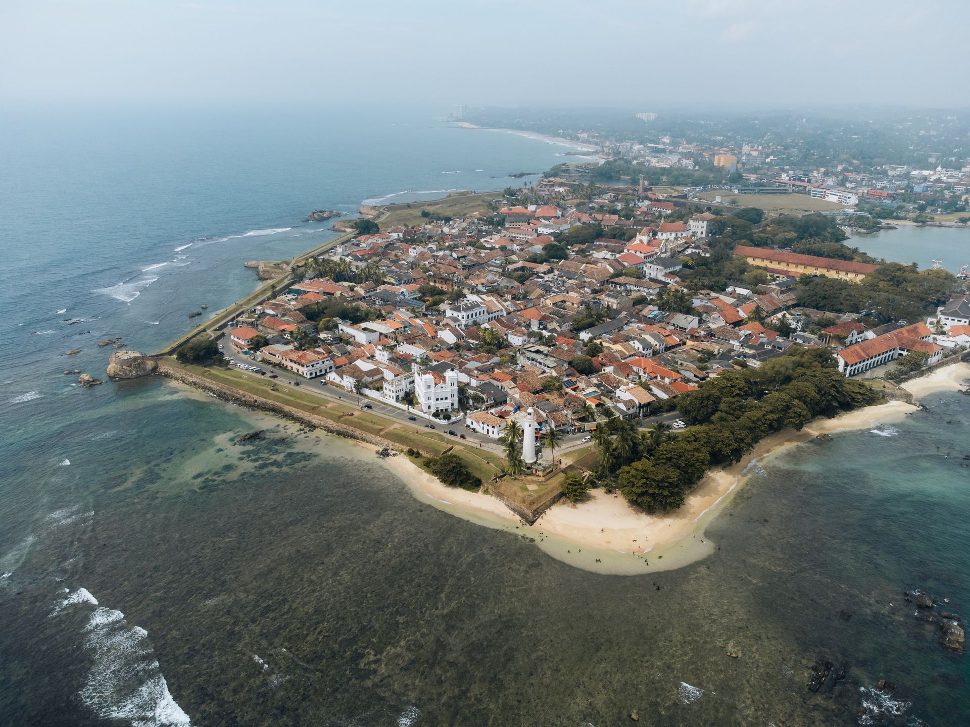 Aerial view of a coastal town with red-roofed houses, rocky shoreline, and calm blue sea.