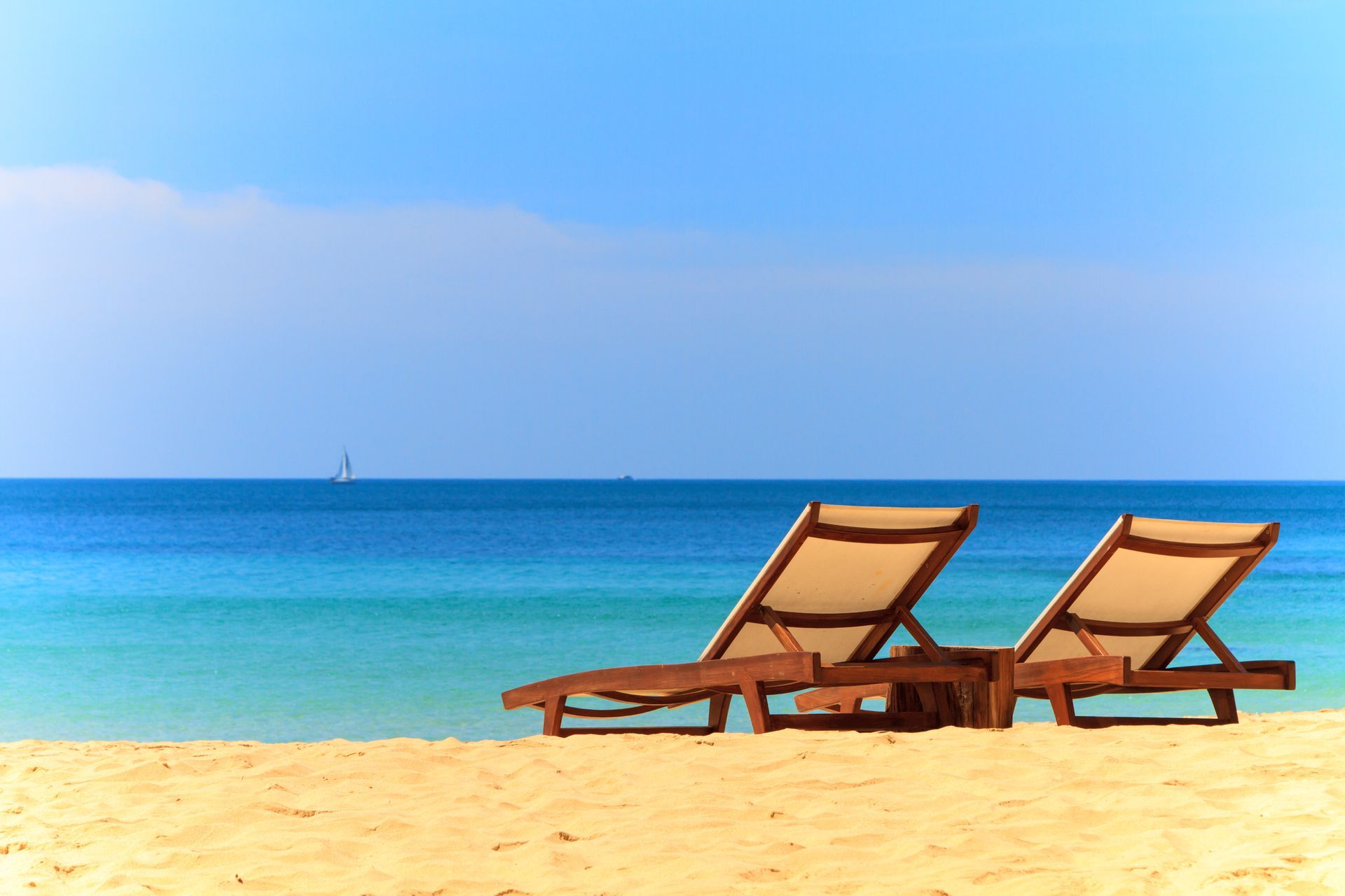 Two wooden lounge chairs on a sandy beach beside a calm blue sea under a clear sky