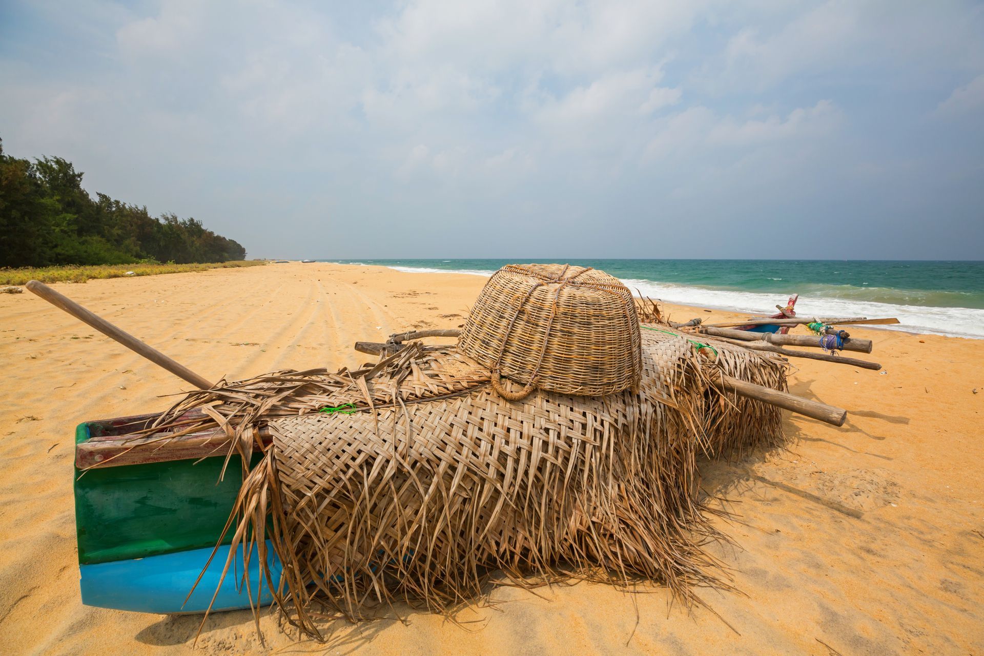 Small wicker fishing boat on a sandy beach with ocean waves and a few people in the distance