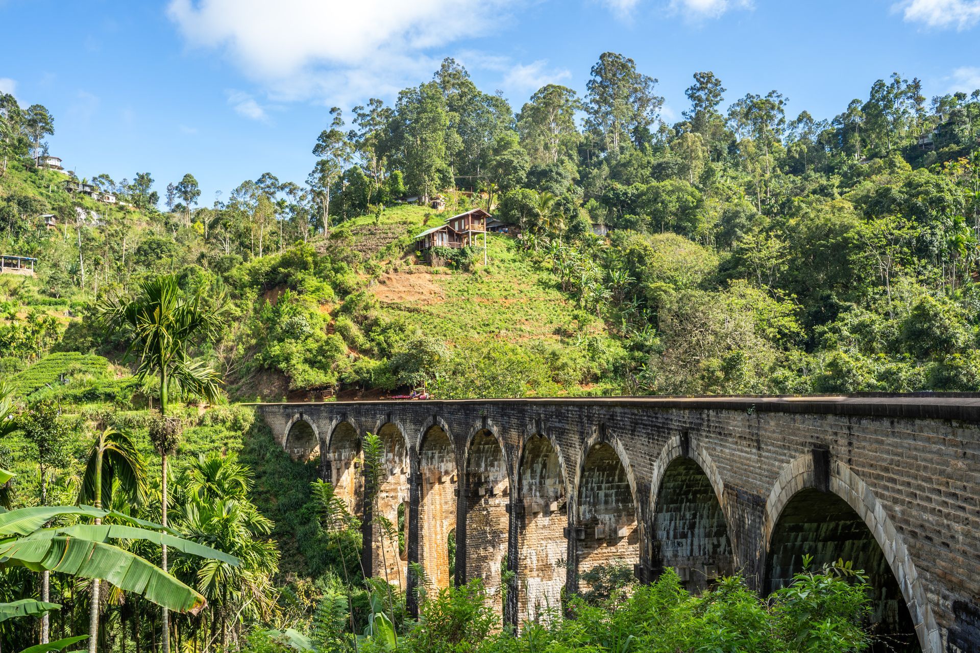 Stone railway viaduct curving through lush green hillside under a bright blue sky