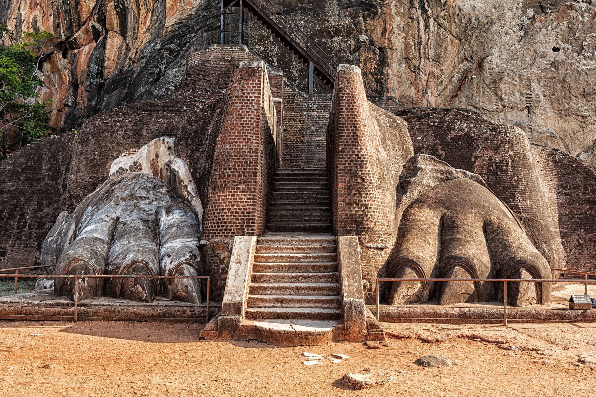 Stone staircase carved into a cliff between giant lion paws, with a rocky mountain backdrop.