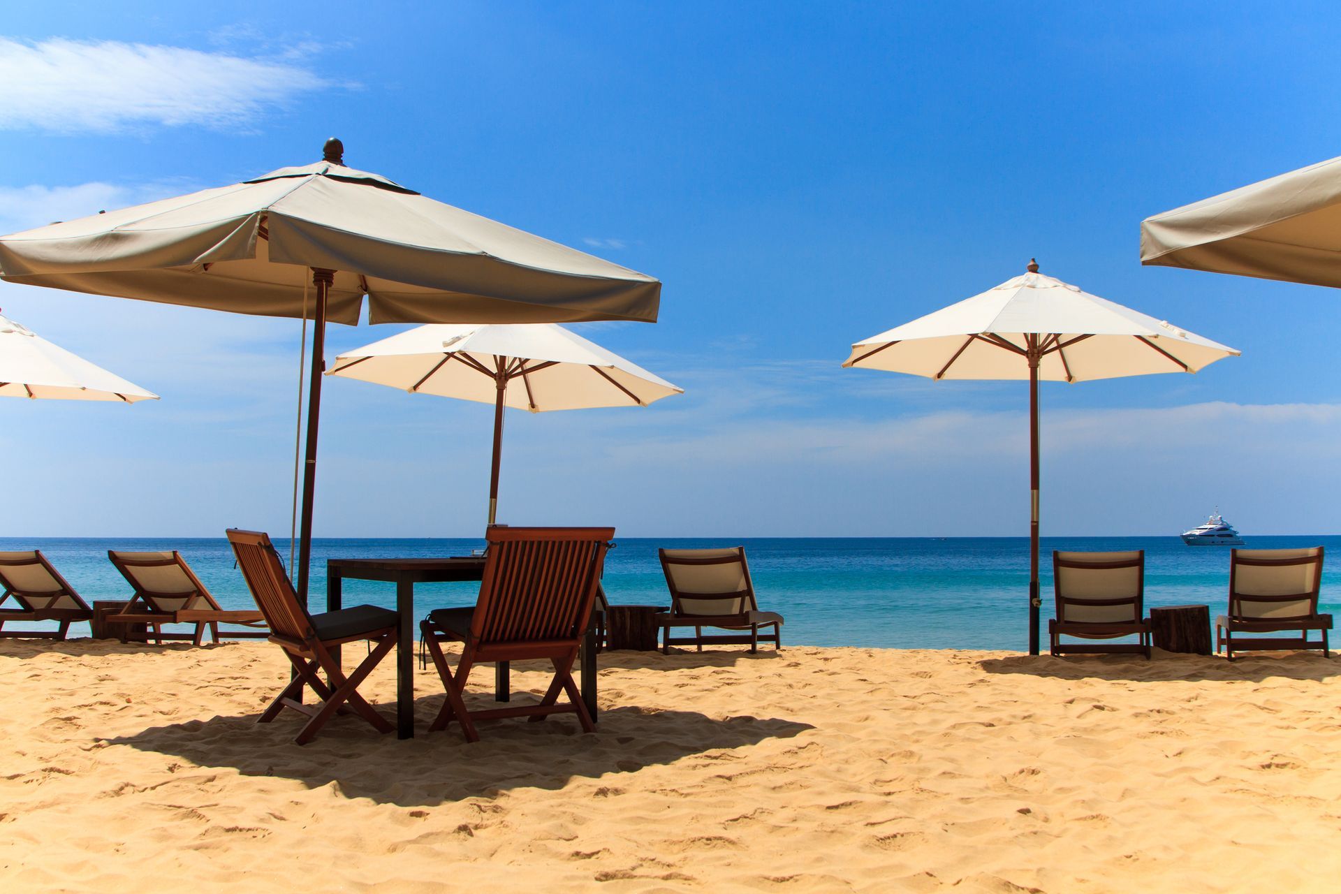 Sunny beach with beige umbrellas and wooden lounge chairs facing a calm blue sea