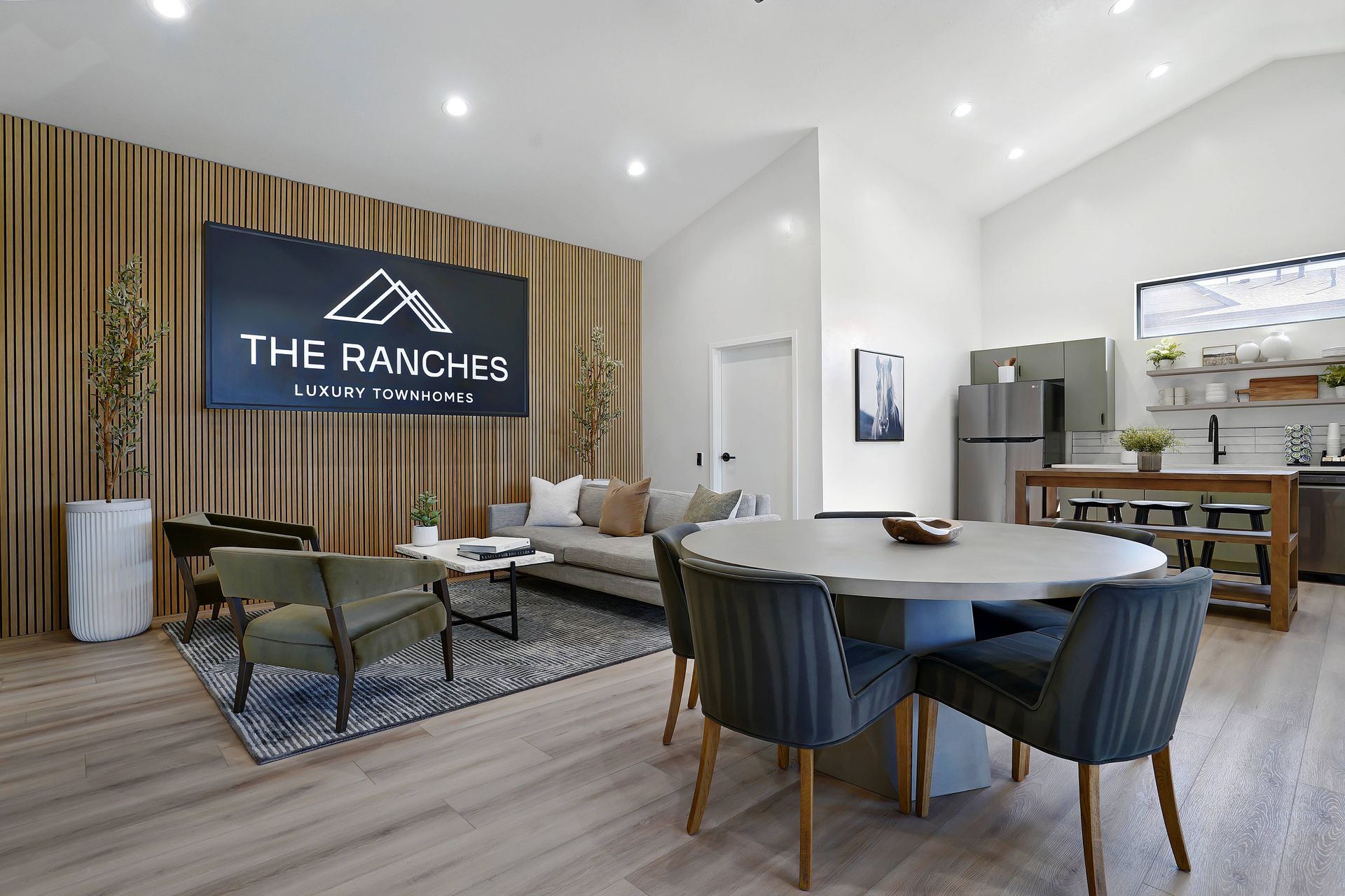 A modern lounge area with seating, a kitchen, and a large screen displaying