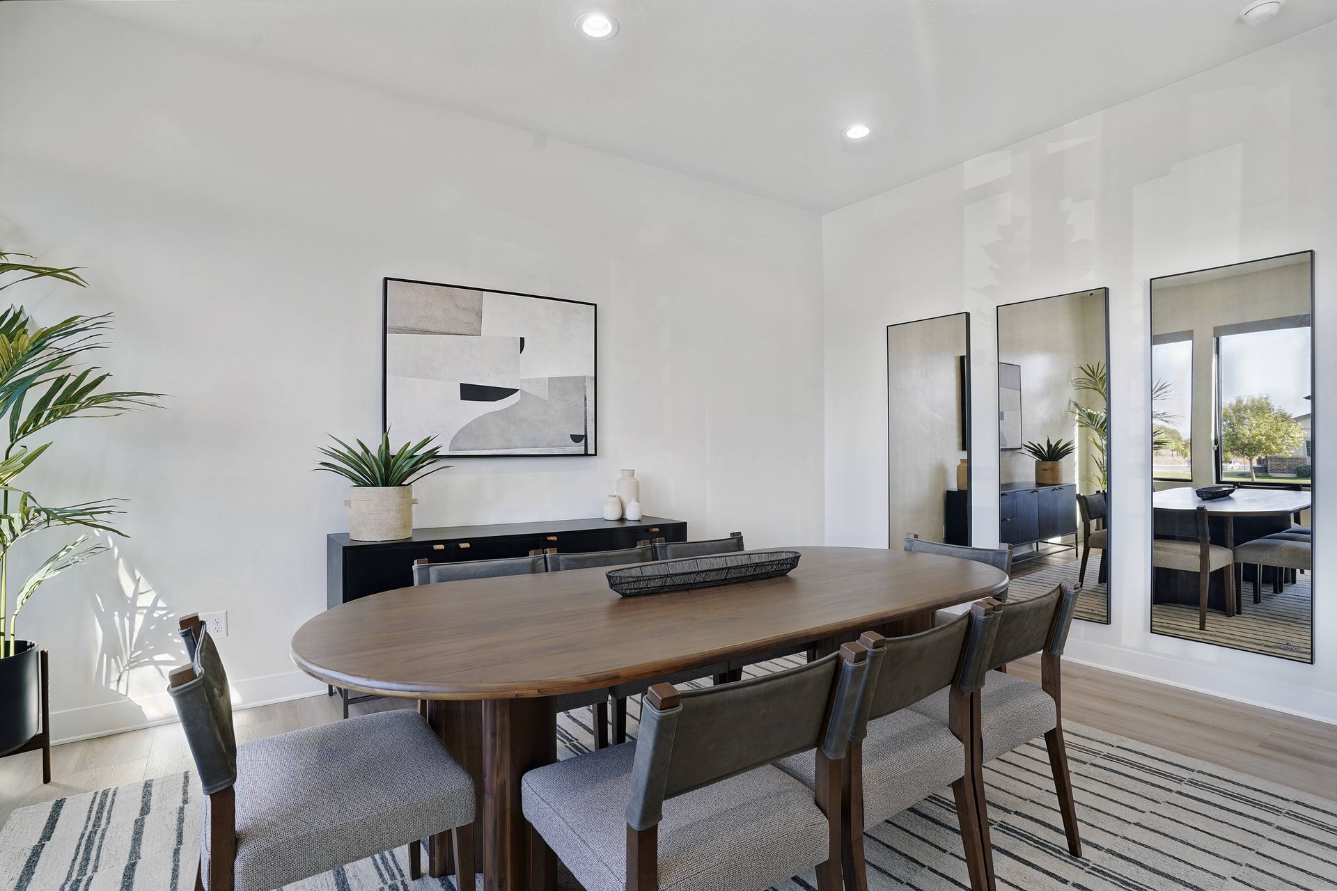 Dining room with oval wooden table, six chairs, and artwork on a white wall.
