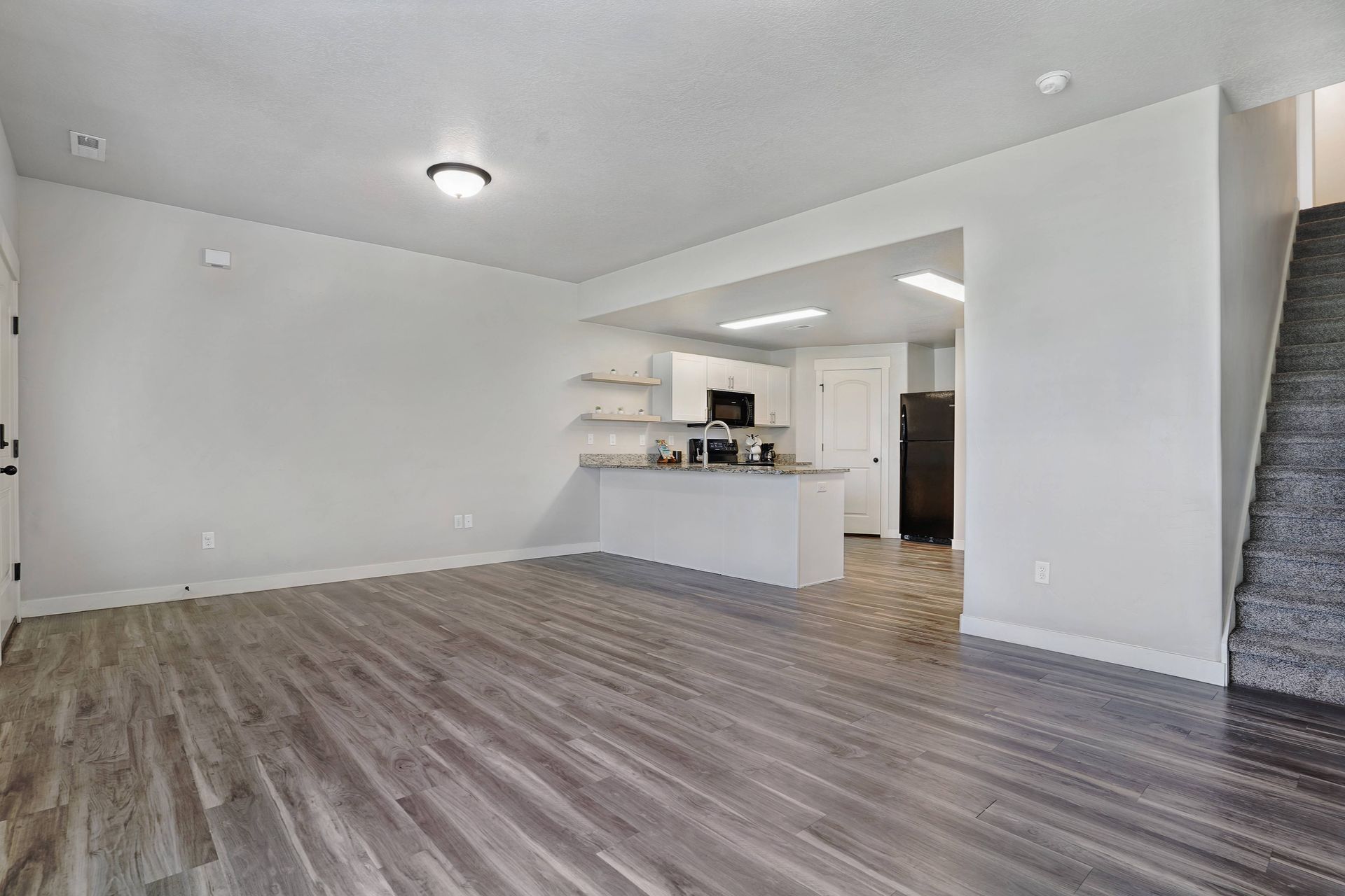 Empty living space with wood flooring, kitchen, and stairs.