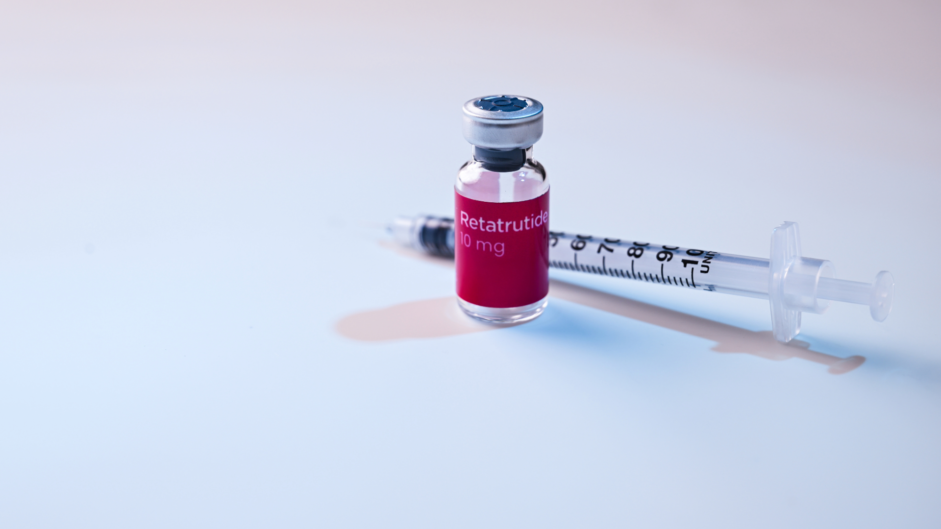 Red vial and syringe on a white surface, with a small spill nearby