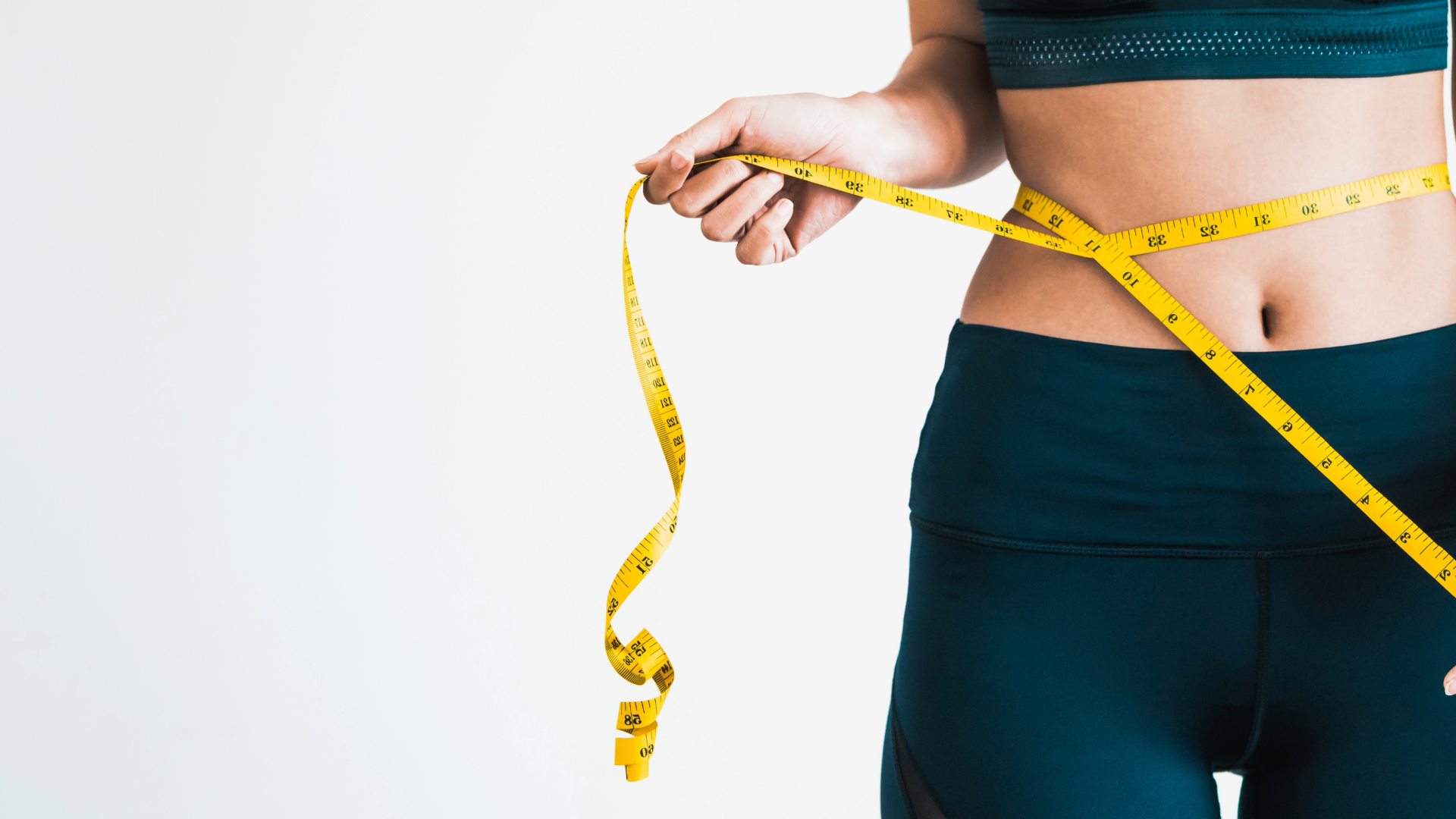 Person measuring their waist with a yellow tape measure, wearing dark athletic clothing.