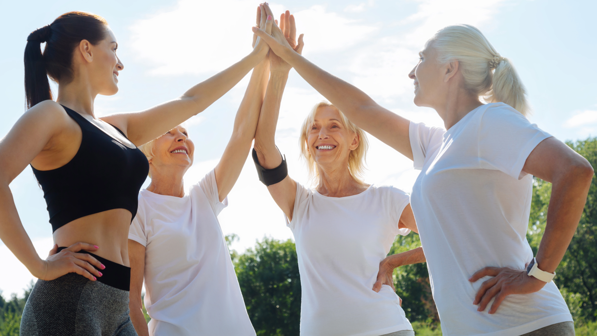 Four people outdoors high-fiving in a circle, smiling under a bright blue sky