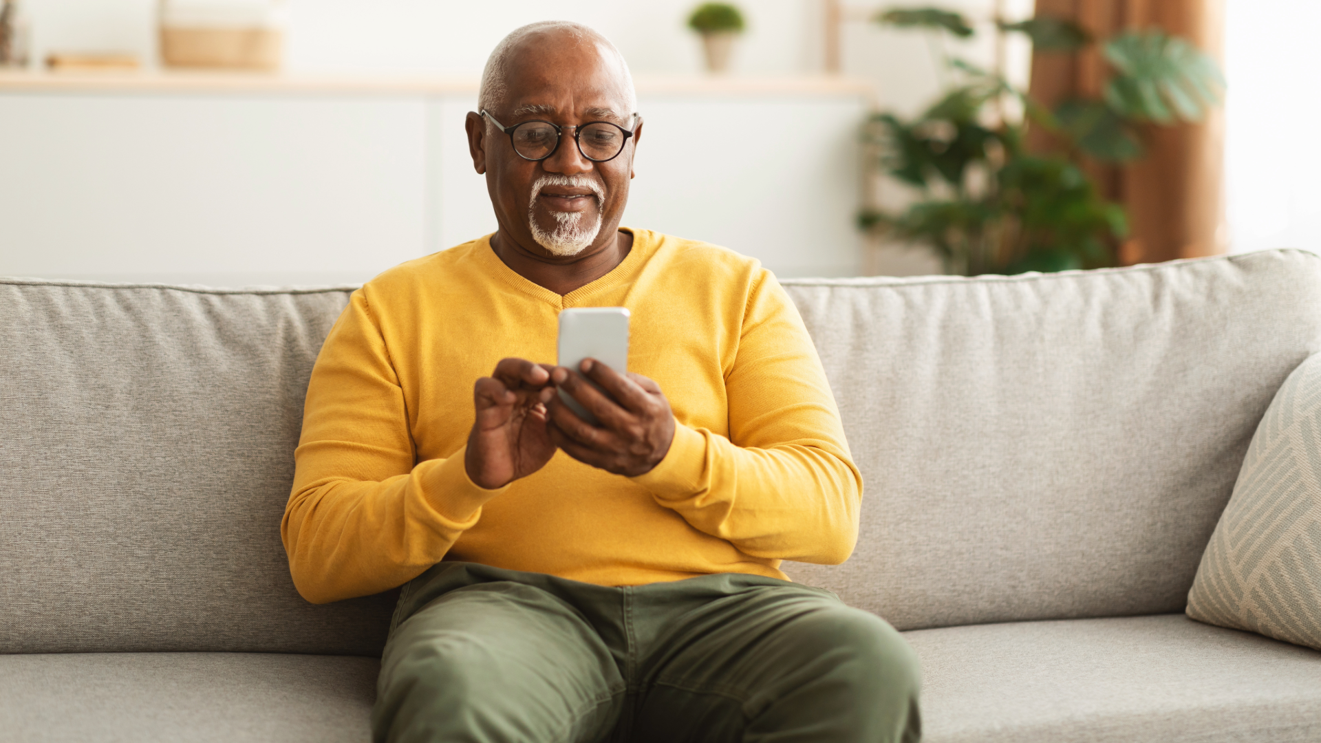 Smiling man on a beige couch using a smartphone in a bright living room