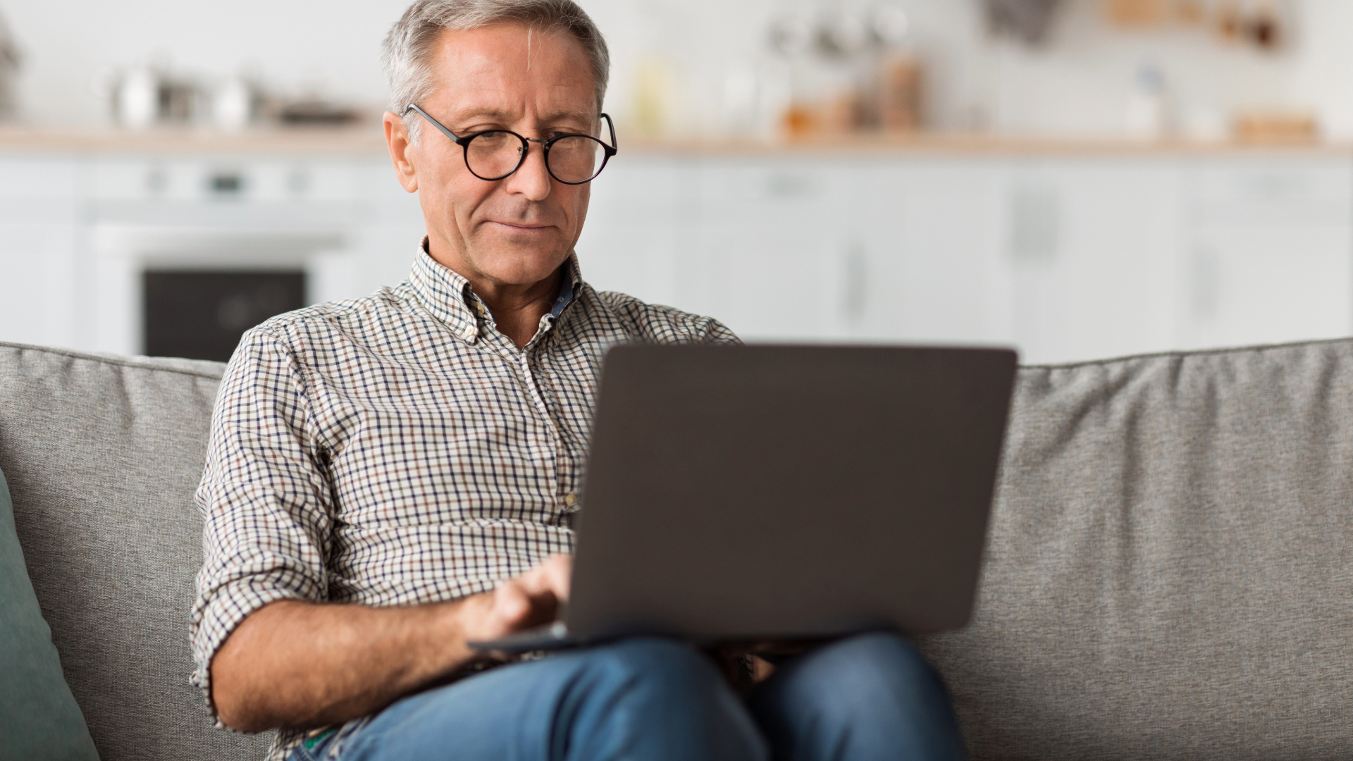 Man sitting on a couch using a laptop in a bright living room