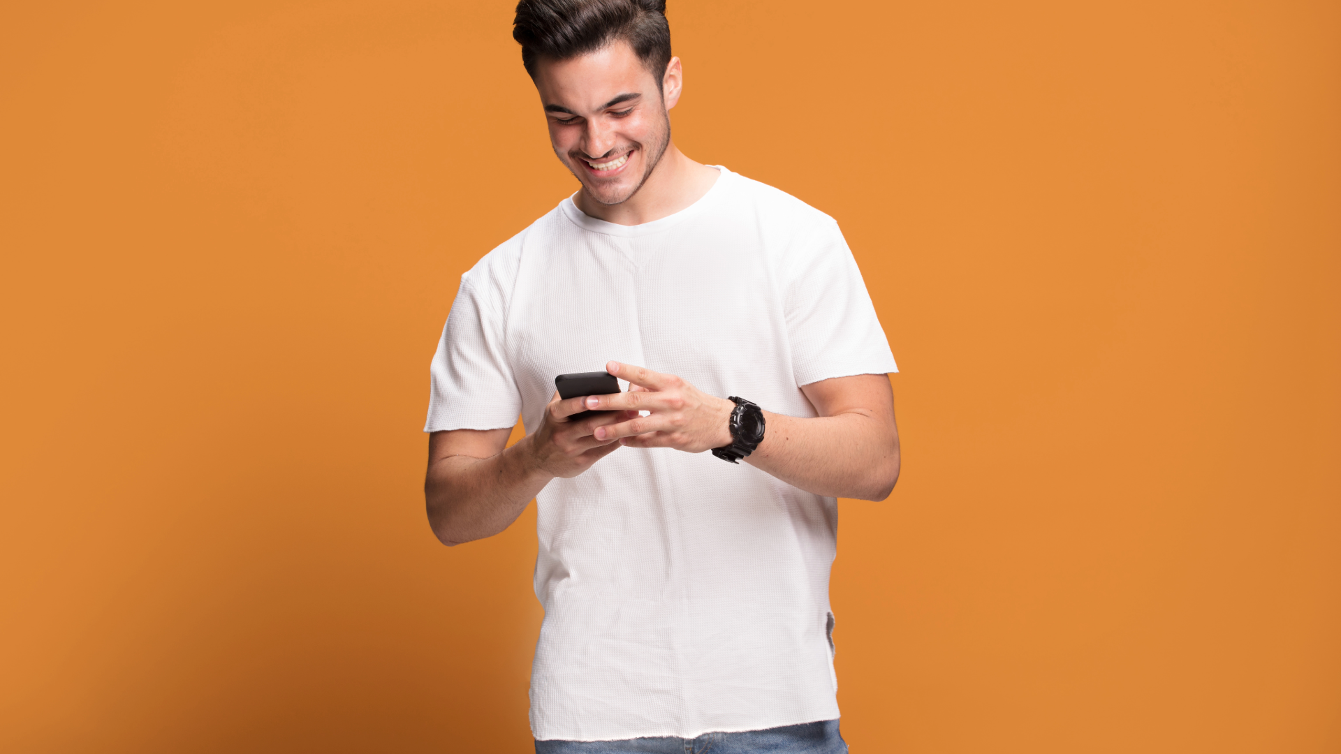 Smiling man in a white T-shirt using a smartphone against an orange background