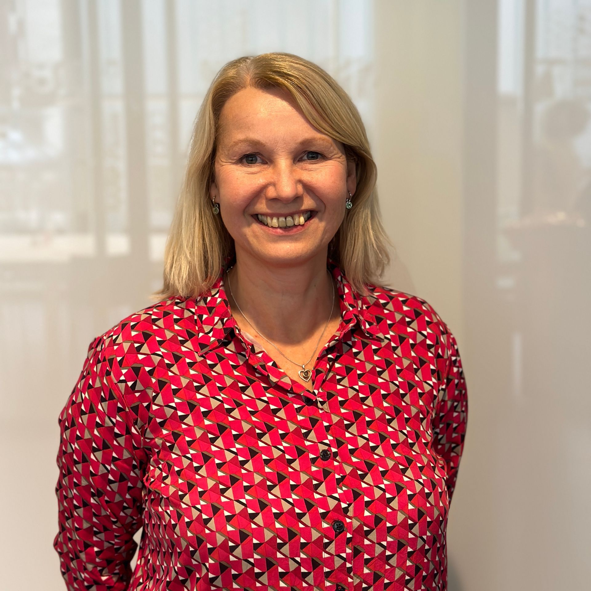 Vrouw met blond haar en een rood, gestreept shirt lacht in een goed verlichte binnenruimte.