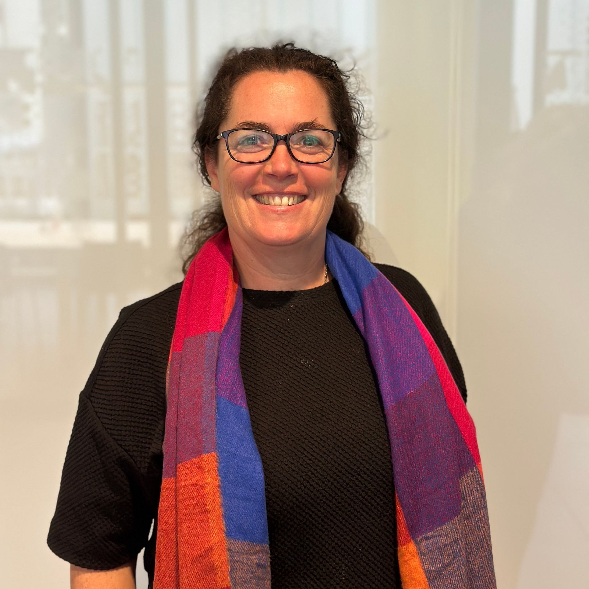 Een vrouw met een bril en een kleurrijke sjaal lacht.