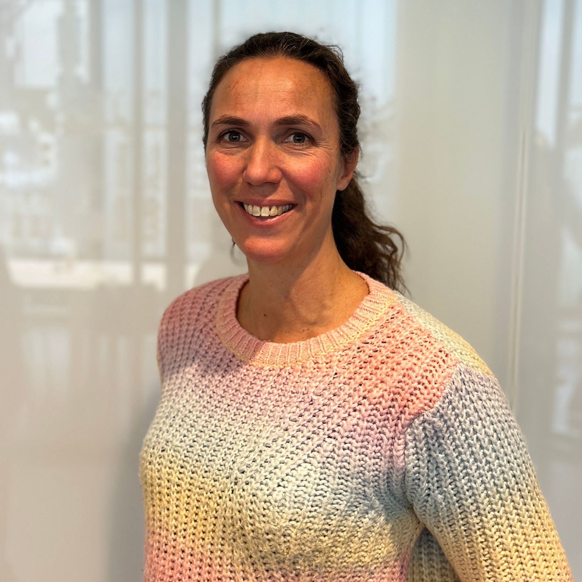 Vrouw in een regenboogkleurige trui lacht. Binnen, tegen een witte achtergrond.