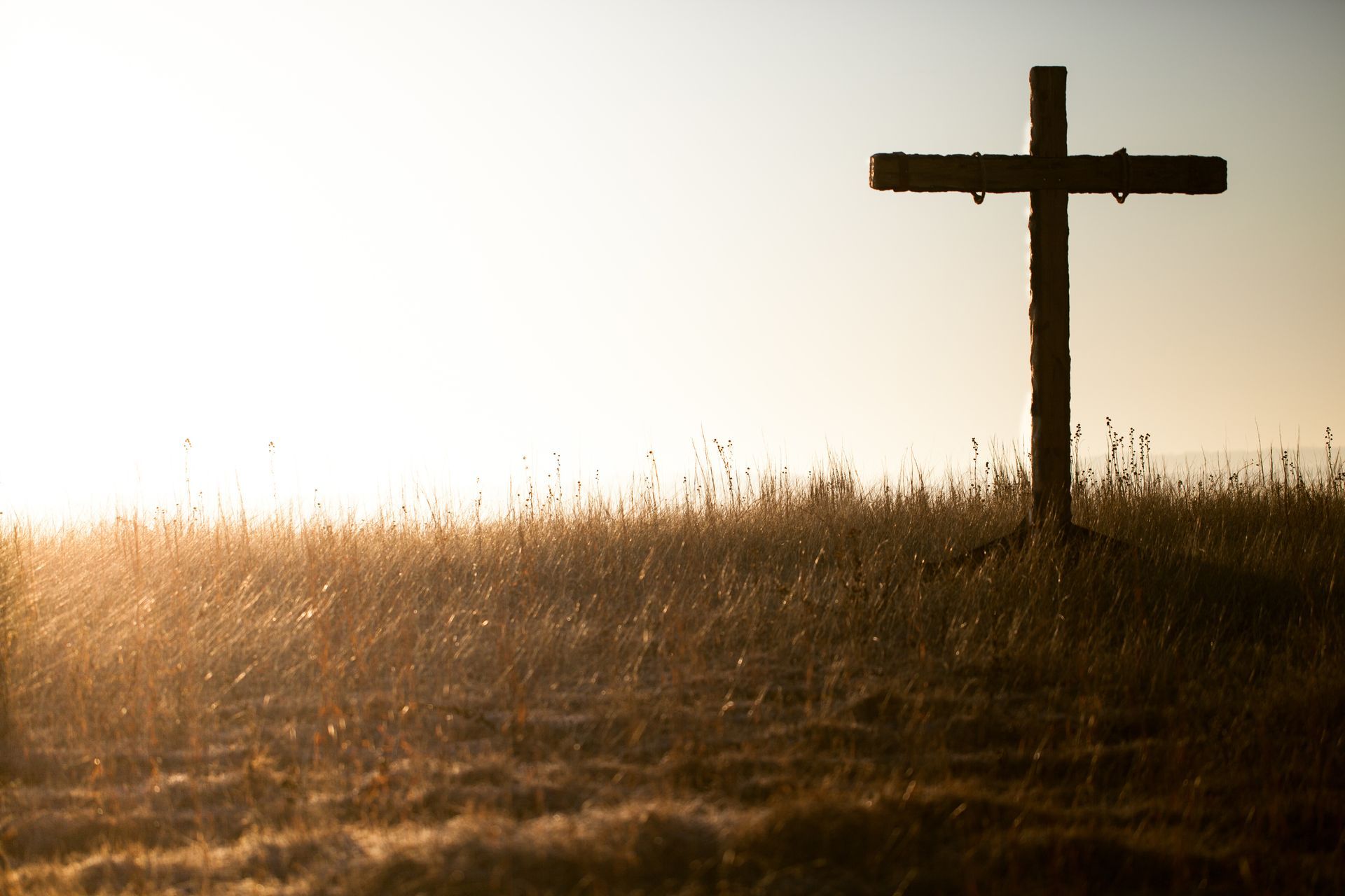 Silhouetted wooden cross in a grassy field at sunrise