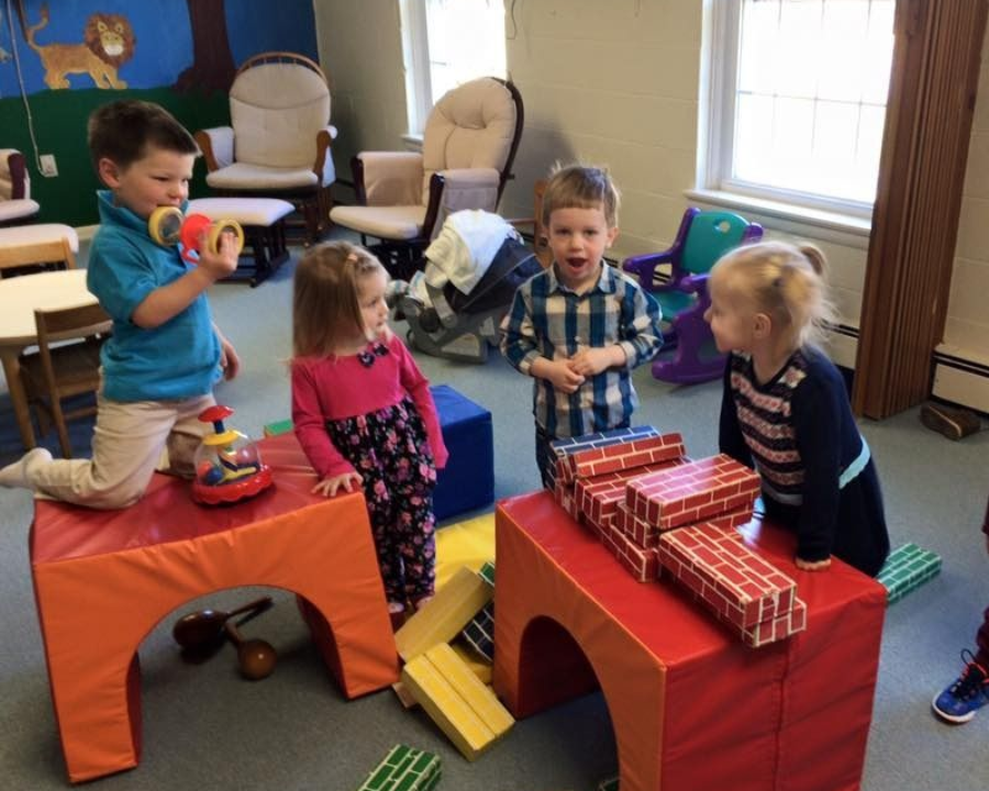 Children playing with toy blocks and chairs in a colorful classroom area
