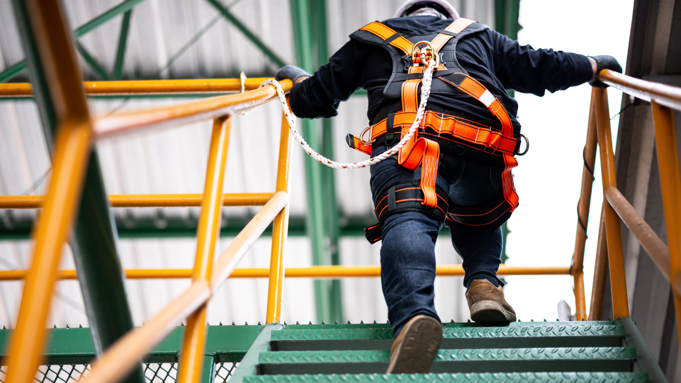 A man wearing a safety harness is walking up a set of stairs.