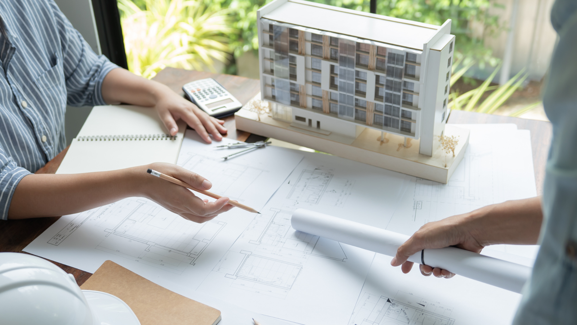 A couple of people are sitting at a table with a model of a building.