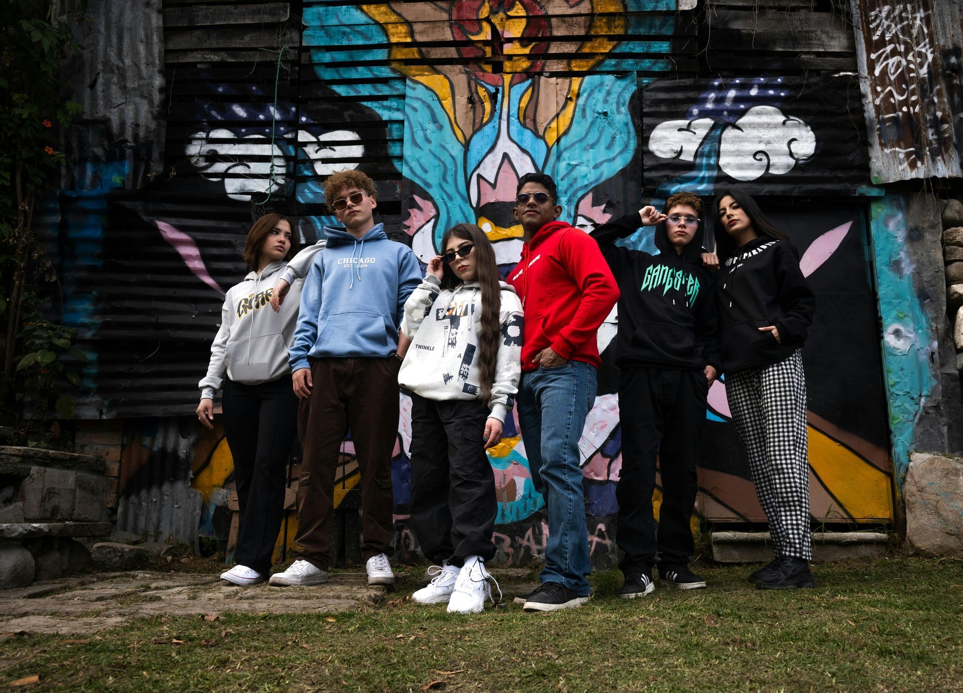 Group of six posing in front of a colorful graffiti mural outdoors