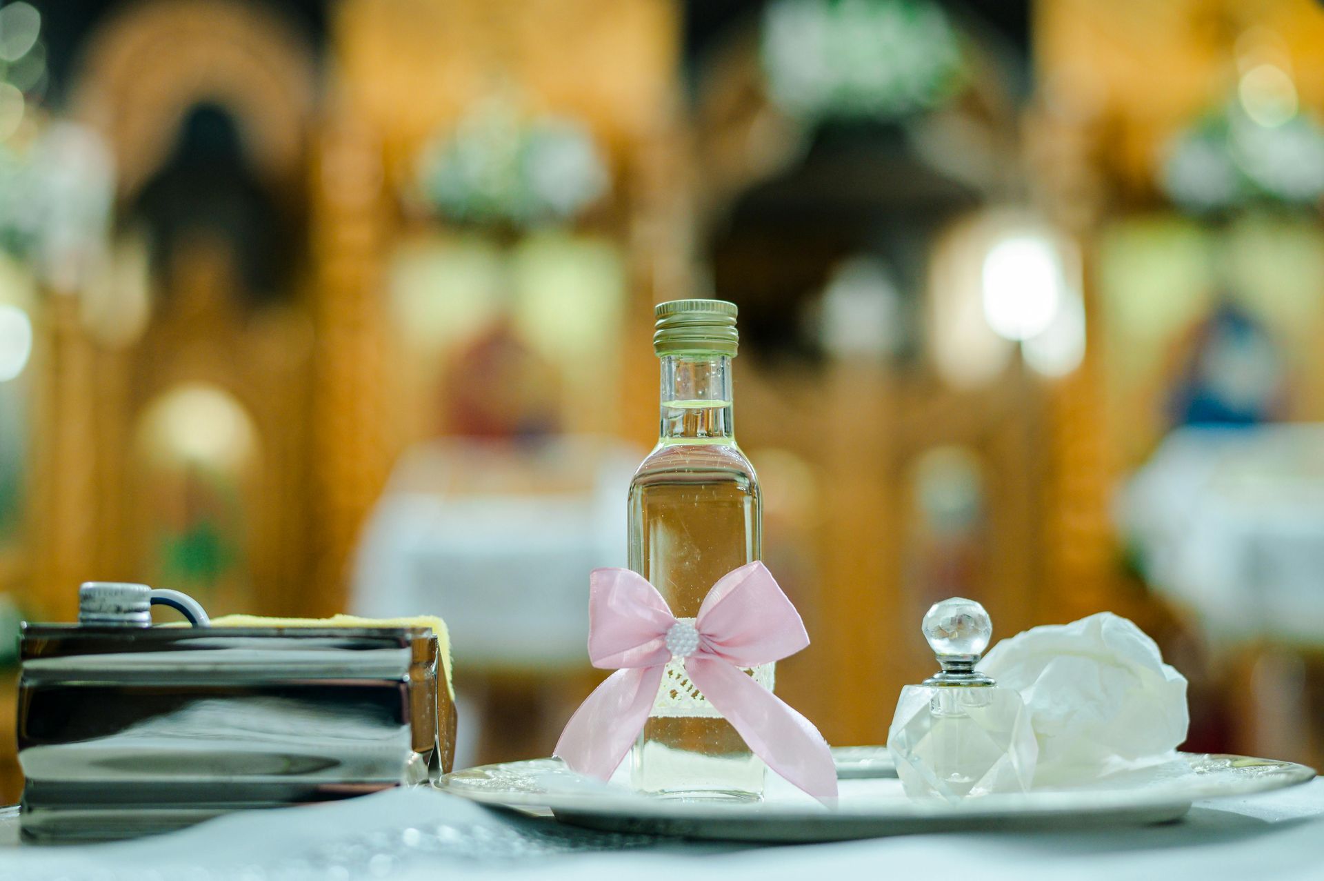 Small perfume bottle with pink bow on a tray, beside folded towels in a softly blurred spa setting