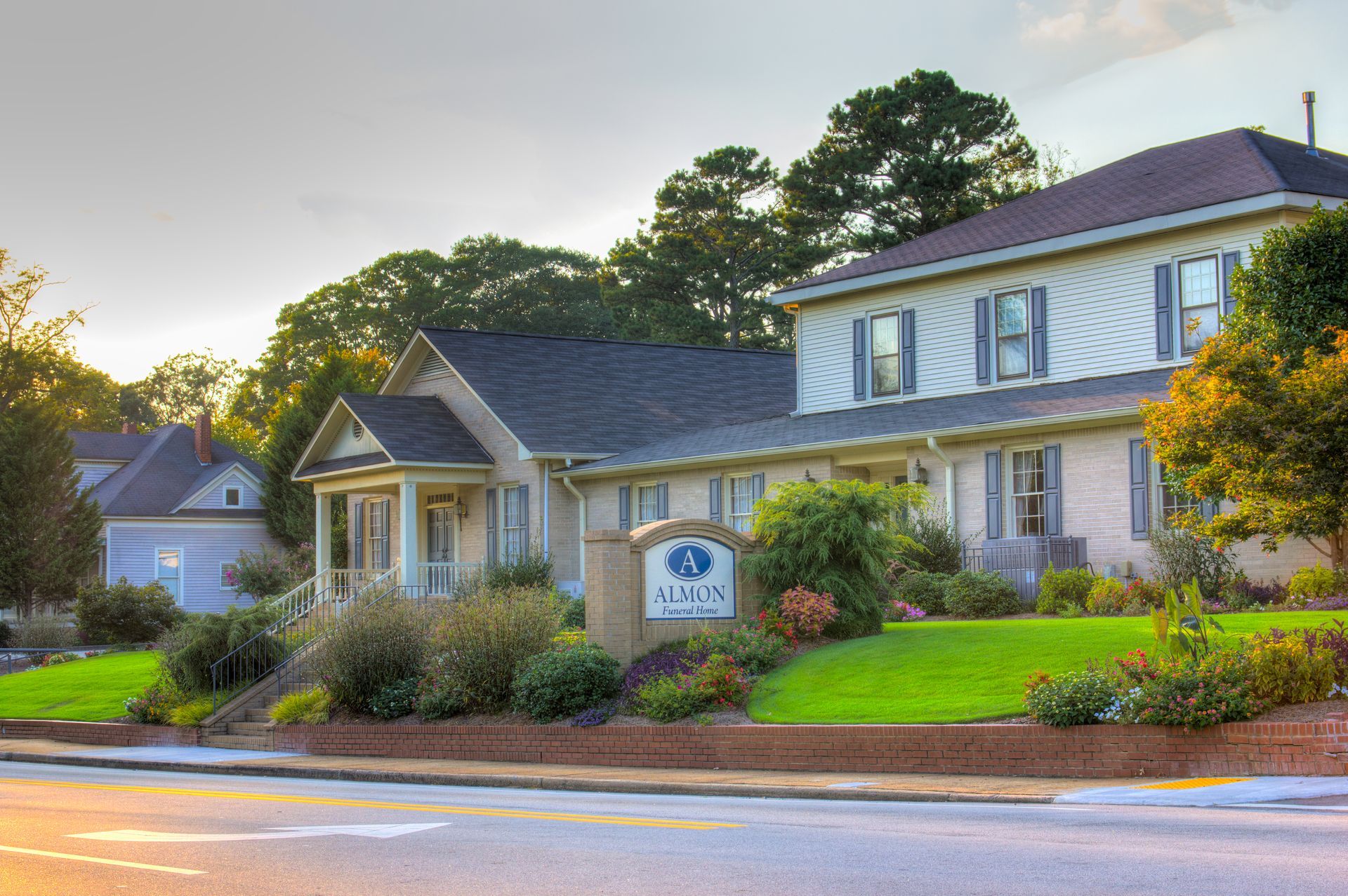 Suburban office building with a blue sign, landscaped shrubs, and a road in front at sunset