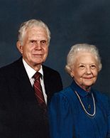 Portrait of an elderly couple in formal attire, posed against a dark background.