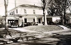 Black-and-white photo of a two-story house with a porch and trees in front.