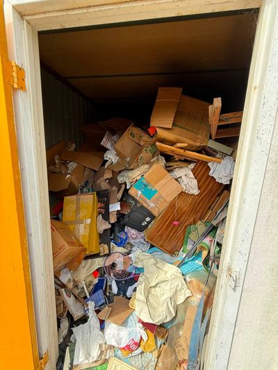 Overflowing storage closet filled with piles of cardboard, papers, and miscellaneous clutter