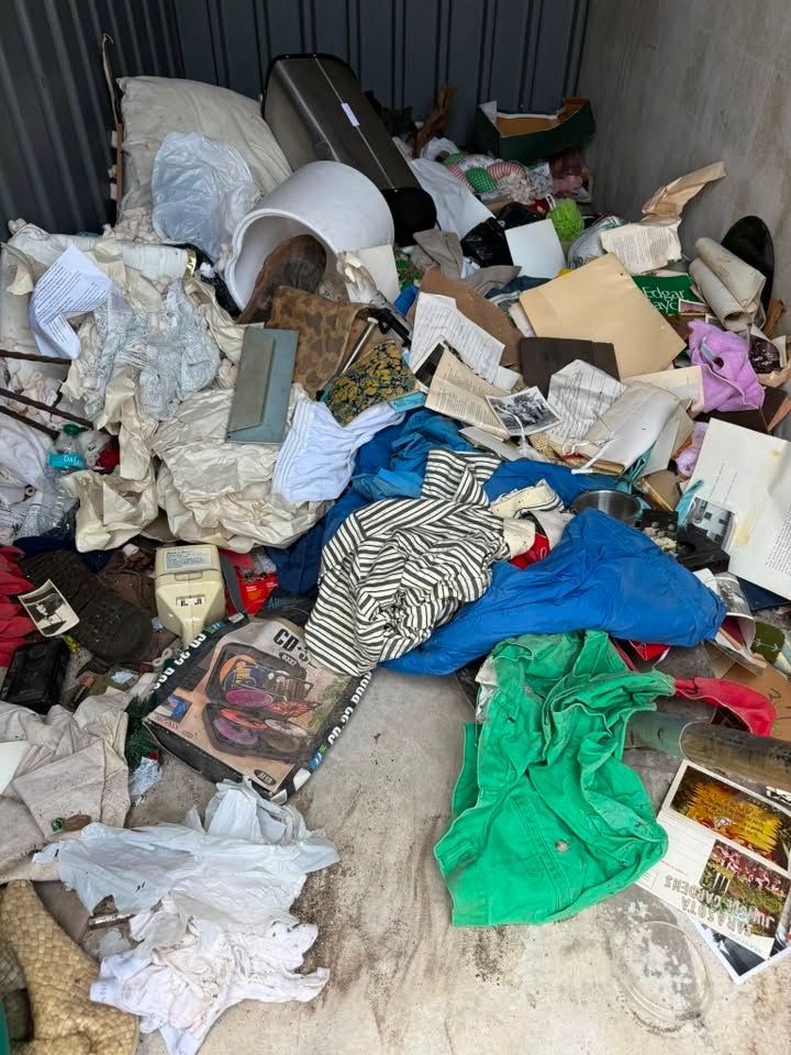 Cluttered room with piles of trash, clothes, cardboard, and household debris on the floor