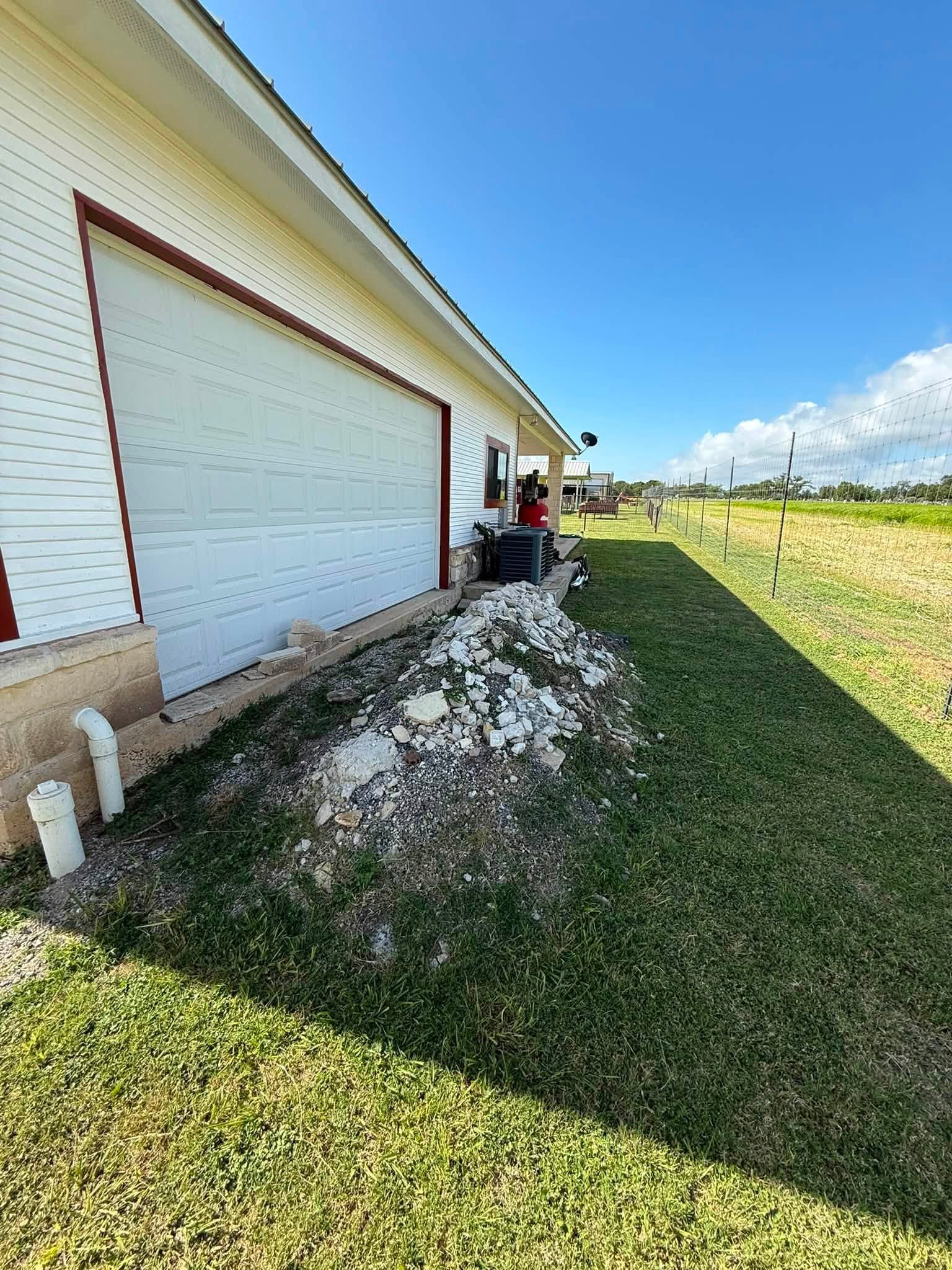 House side with a white garage door, gravel strip, and green lawn under a bright blue sky.