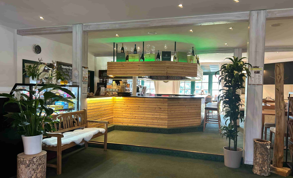 Barbereich des Restaurants Platzhirsch in Olching mit Holztheke, Sitzbank und grüner Beleuchtung.