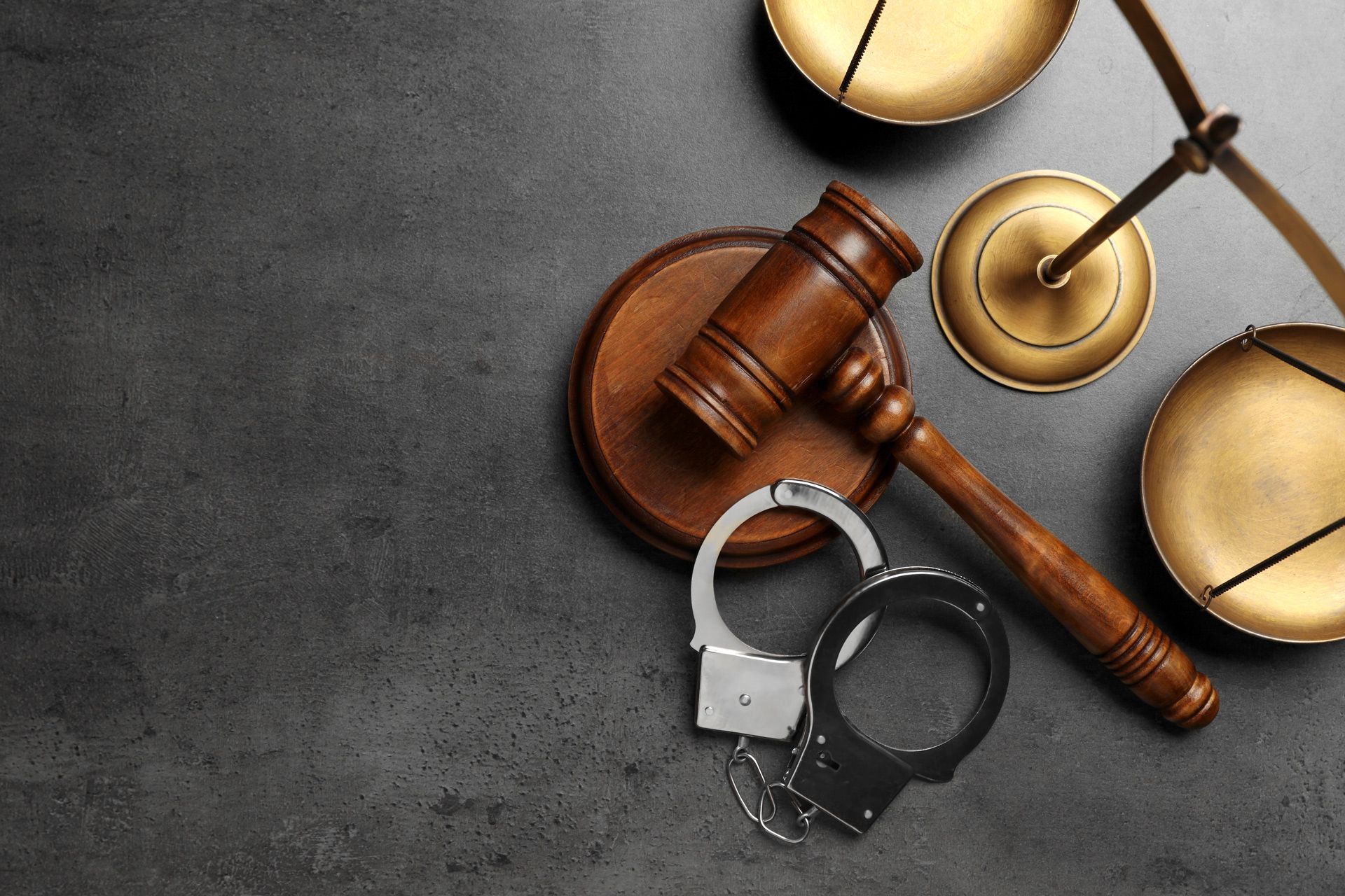 Gavel, handcuffs, and scales of justice arranged on a dark surface representing a legal case. Gavel, handcuffs, and scales of justice arranged on a dark surface representing a legal case.