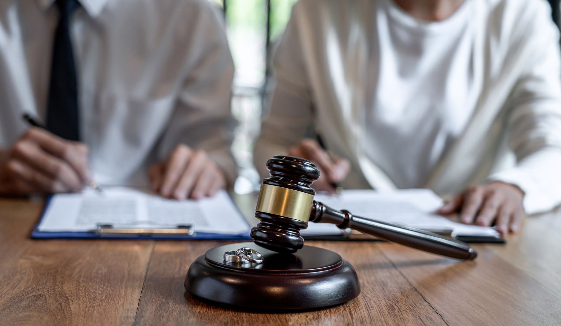 Wedding rings resting on a judge's gavel with a couple signing papers in the background.
