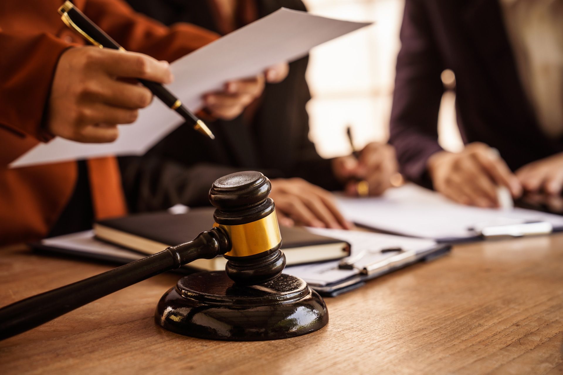 Judge’s gavel on a table as legal professionals review documents together. Judge’s gavel on a table as legal professionals review documents together.