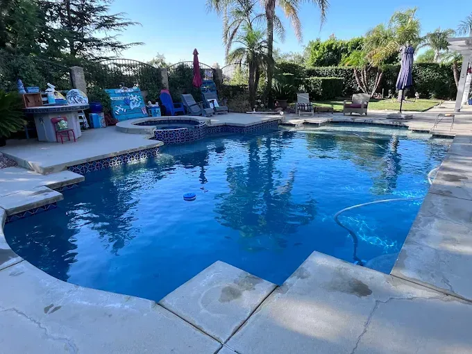 Pool with blue water and surrounding concrete deck; palm trees and lounge chairs in the background.