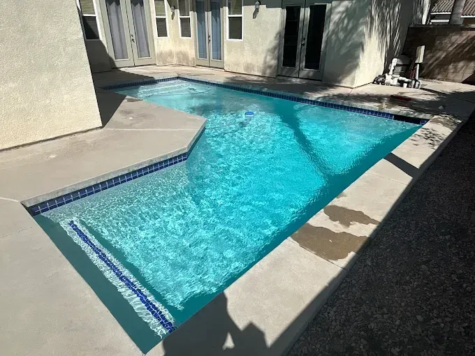 Swimming pool with blue water and tiled edges, surrounded by concrete.