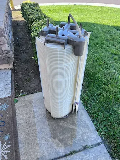 Tall, cylindrical pool filter on a concrete step next to a lawn and garden bed.