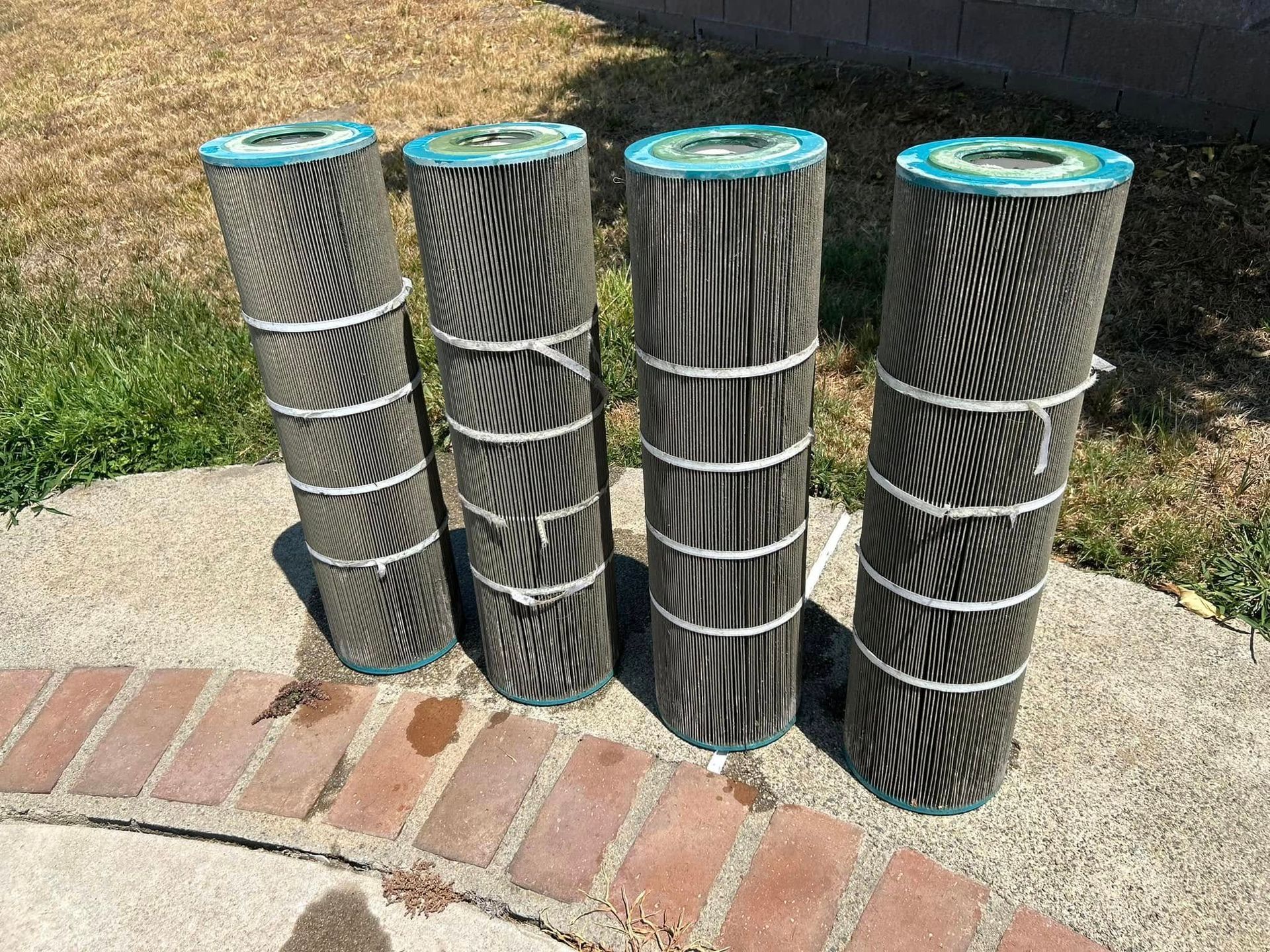 Four cylindrical pool filters, black and white pleated, standing upright on concrete.