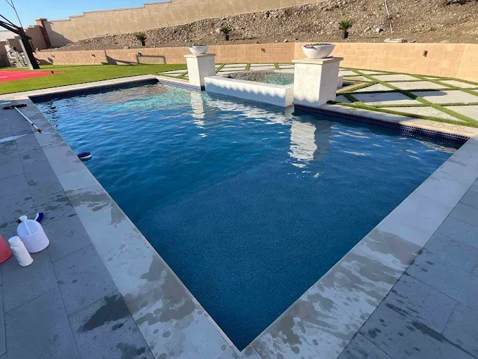 Rectangular pool with blue water, surrounded by gray stone. Small spa in the center with white pillars.