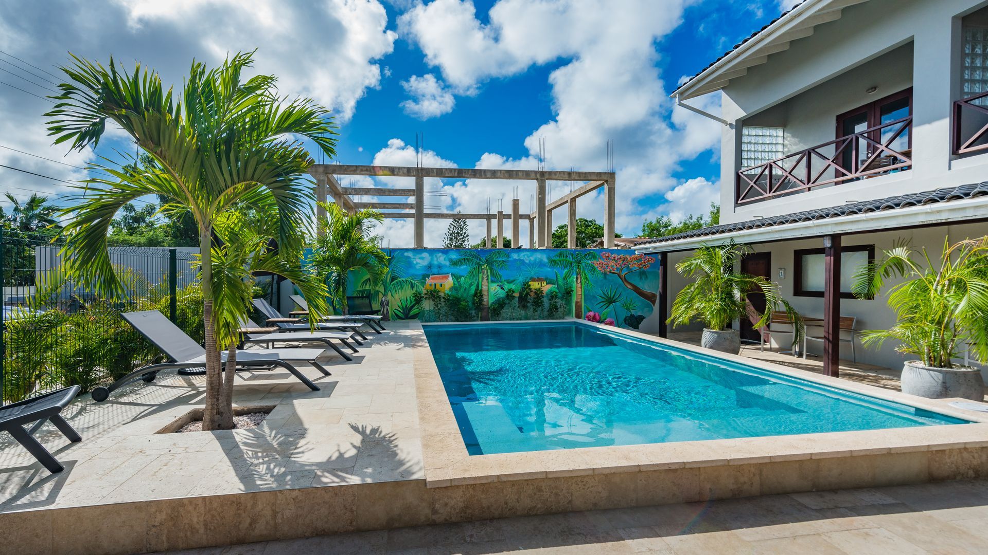 A large swimming pool surrounded by chairs and palm trees in front of a house.