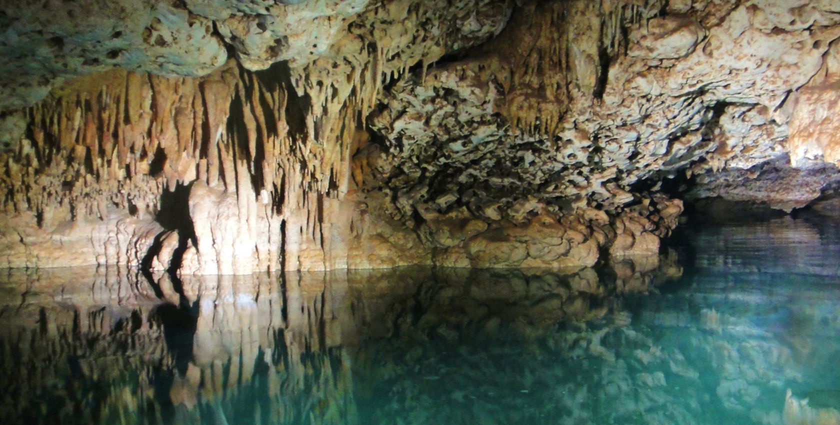 A person is standing in a cave next to a body of water.