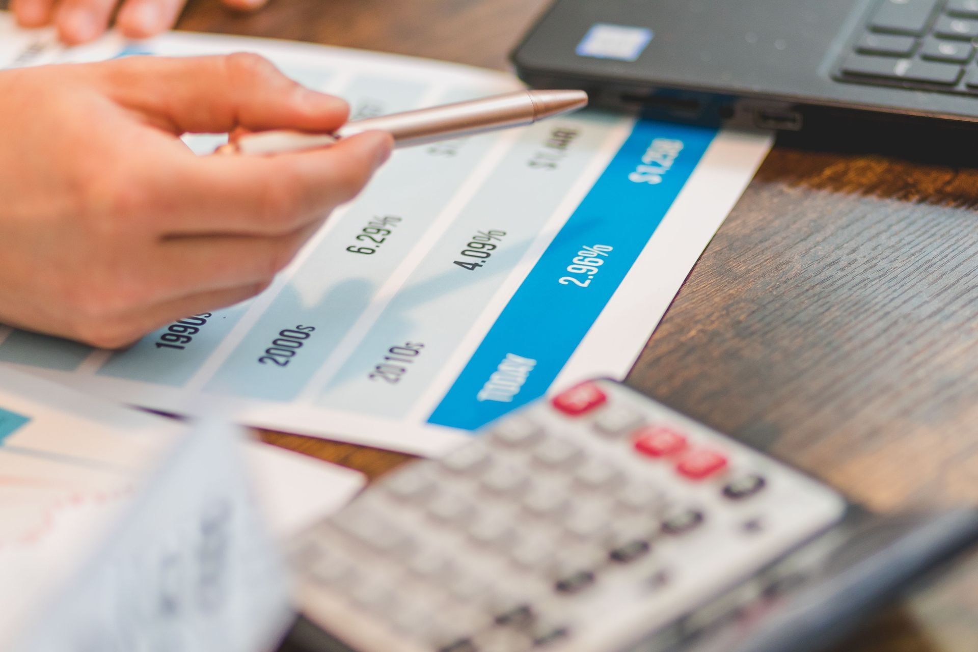Hand holding a stylus over a tablet app with blue buttons and a calculator on a wooden desk