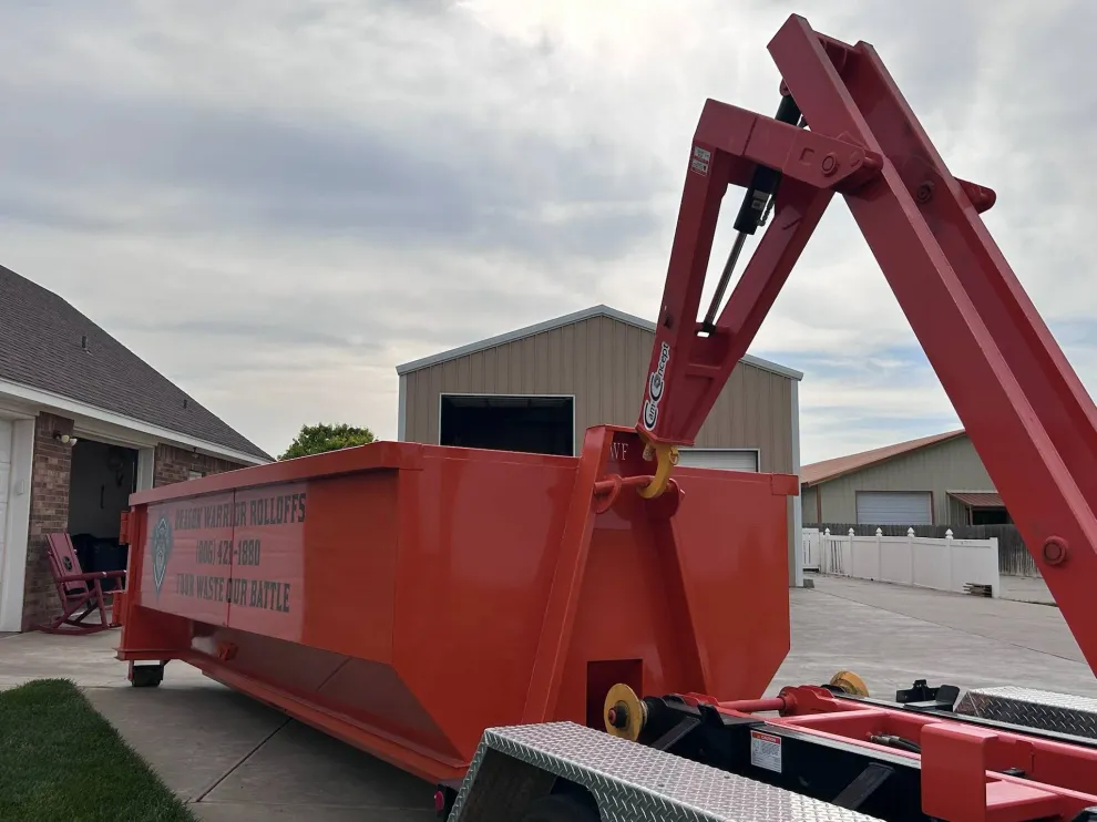 Red dumpster being loaded onto a truck in a residential driveway.