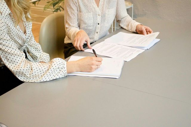 Two people review documents and point at papers across a table.