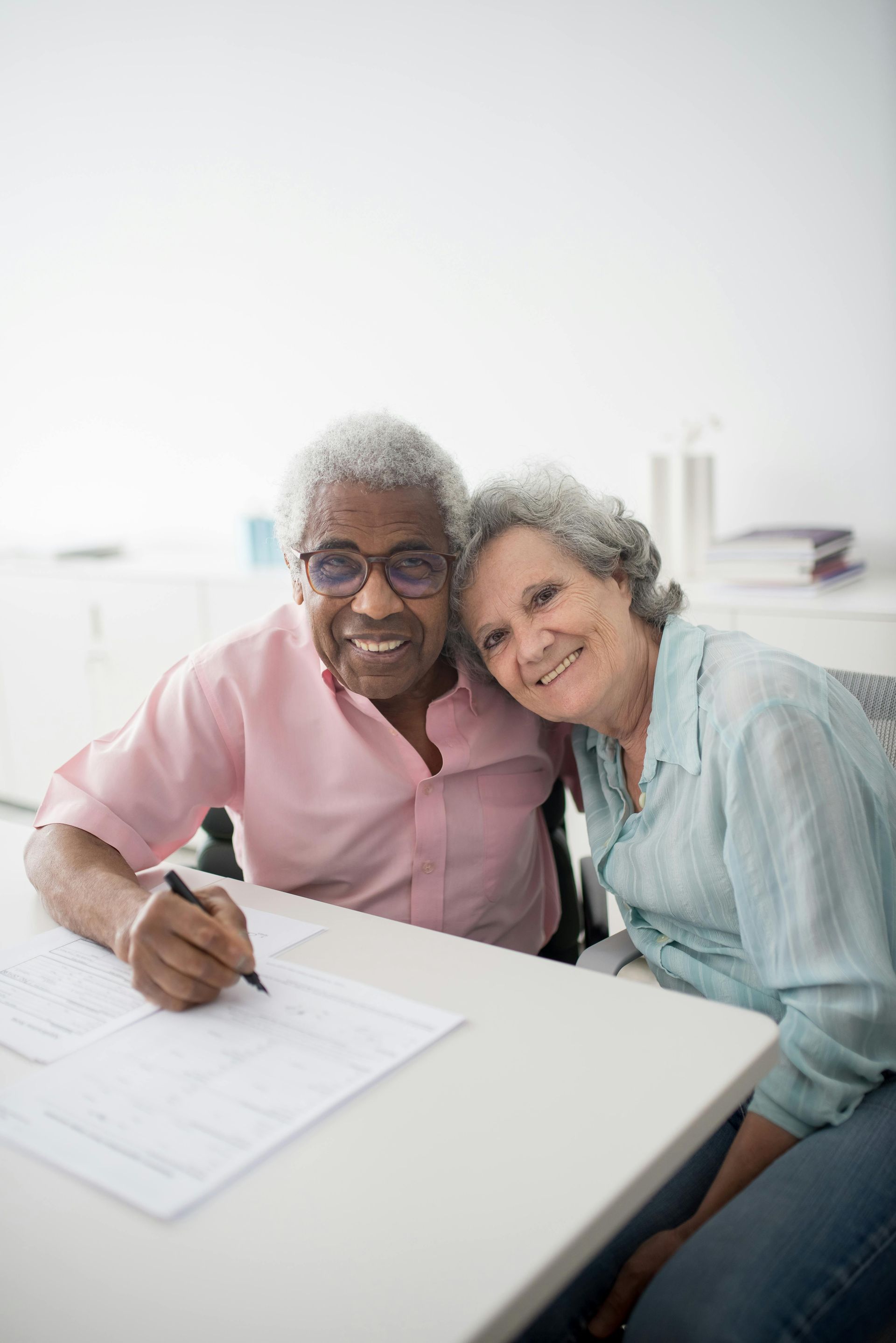 Elderly couple smiles while looking at a laptop on a couch. Woman has arm around man.