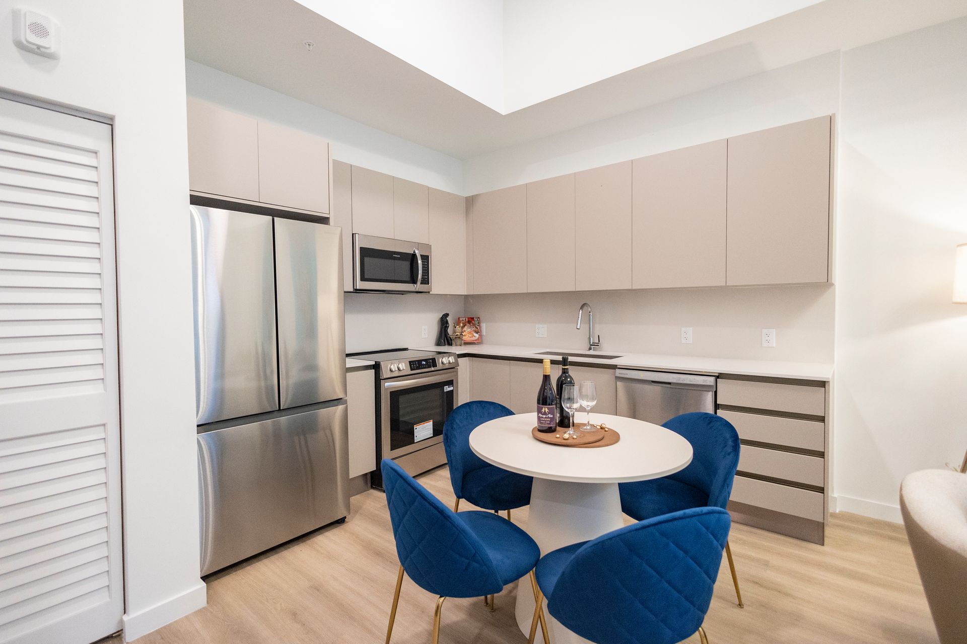 Modern kitchen with stainless steel appliances, beige cabinets, and a small round table with blue chairs at The Arcadian