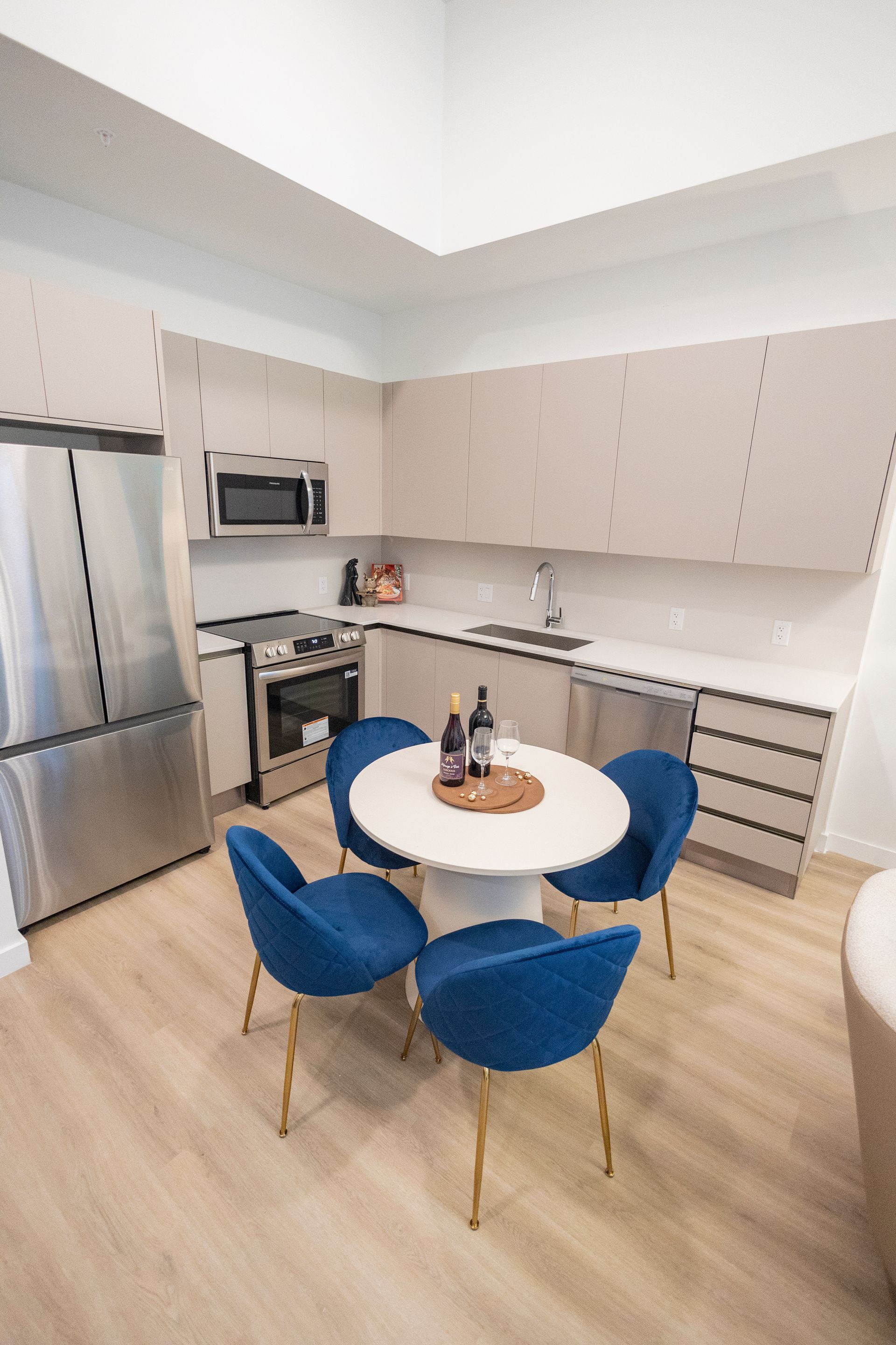 Modern kitchen with stainless fridge, beige cabinets, round white table, and blue chairs at The Arcadian in Fort Lauderdale