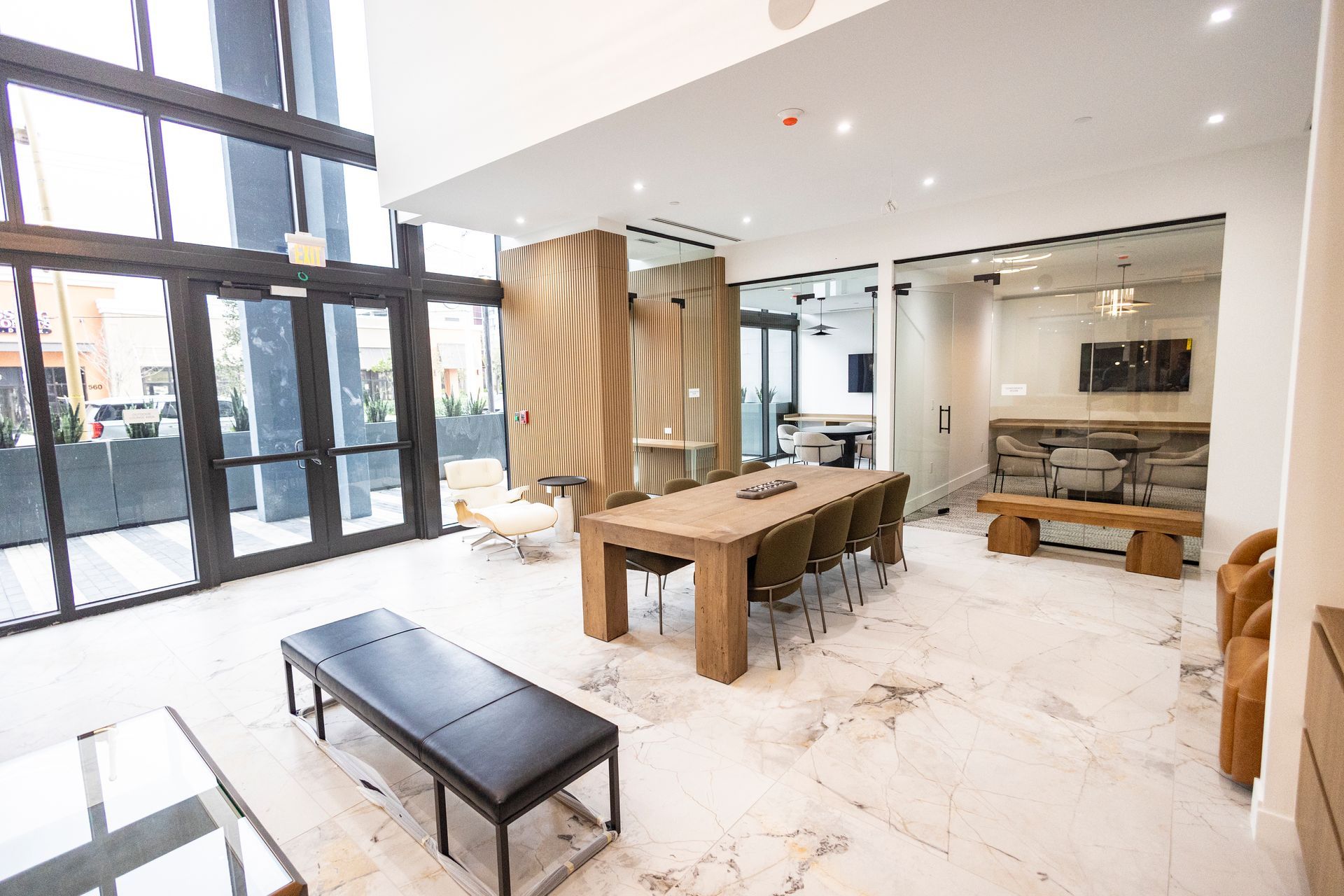Bright modern lobby with marble floor, wooden table, benches, and large glass entrance doors at The Arcadian in Fort Lauderdale