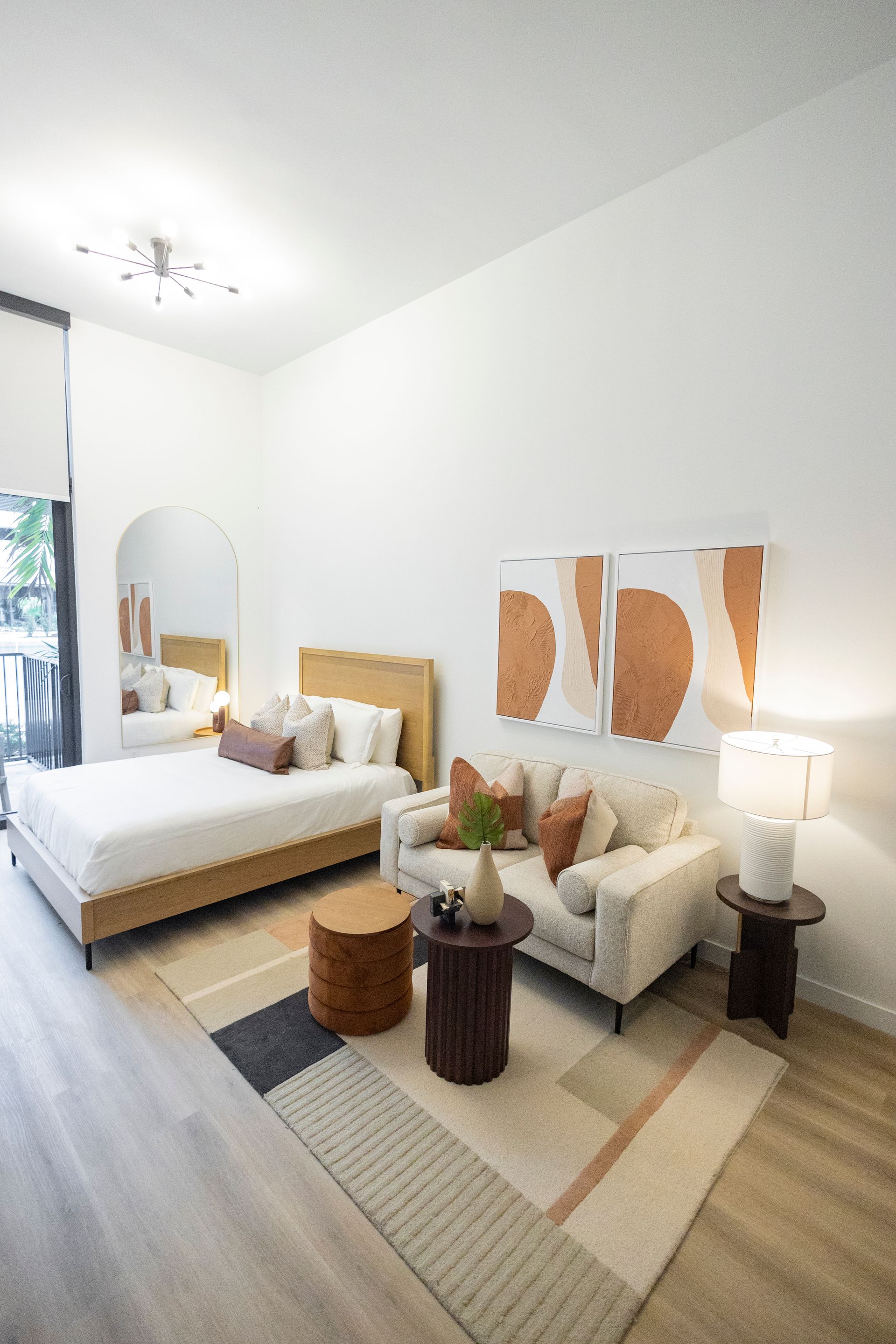 Bright minimalist bedroom with twin beds, cream armchair, abstract wall art, and large window at The Arcadian in Fort Lauderdale