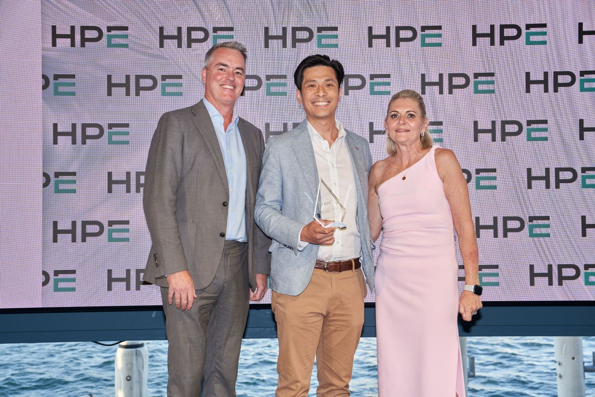 Three people posing for a photo at an HPE event, with an award.  Background has HPE logos.